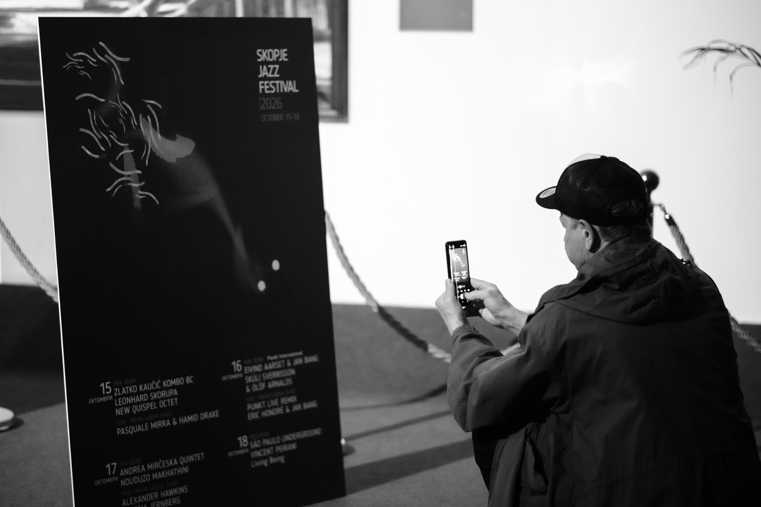 A visitor photographs a Skopje Jazz Festival poster with a phone.