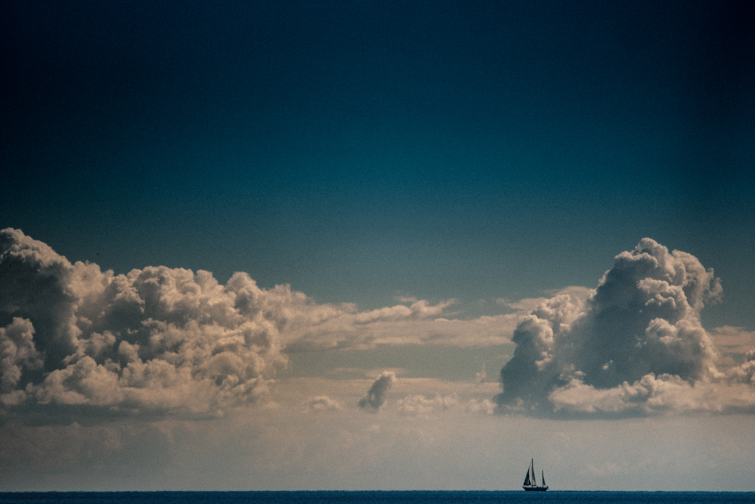 Small sailboat beneath towering clouds over the sea.