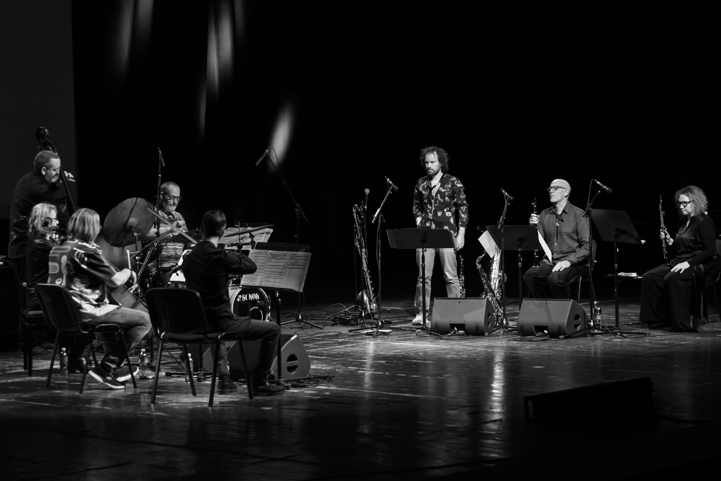 Wide view of a seated musical ensemble and a standing saxophonist on stage.