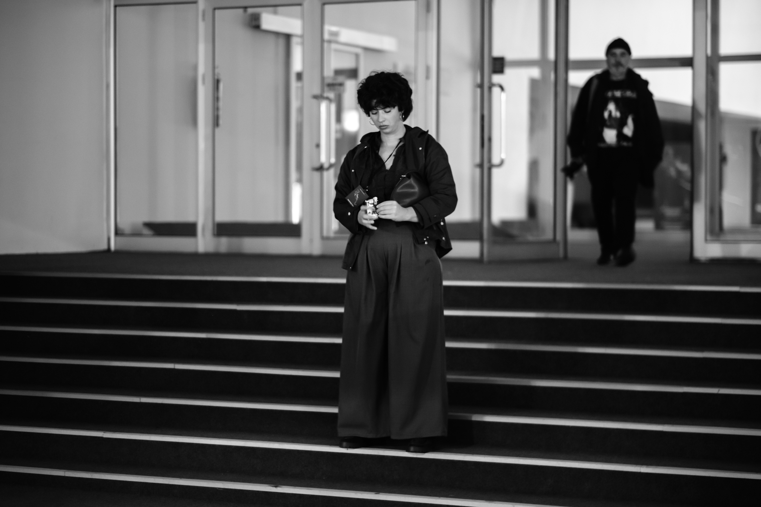 A woman stands on the steps in front of tall glass entrance doors.